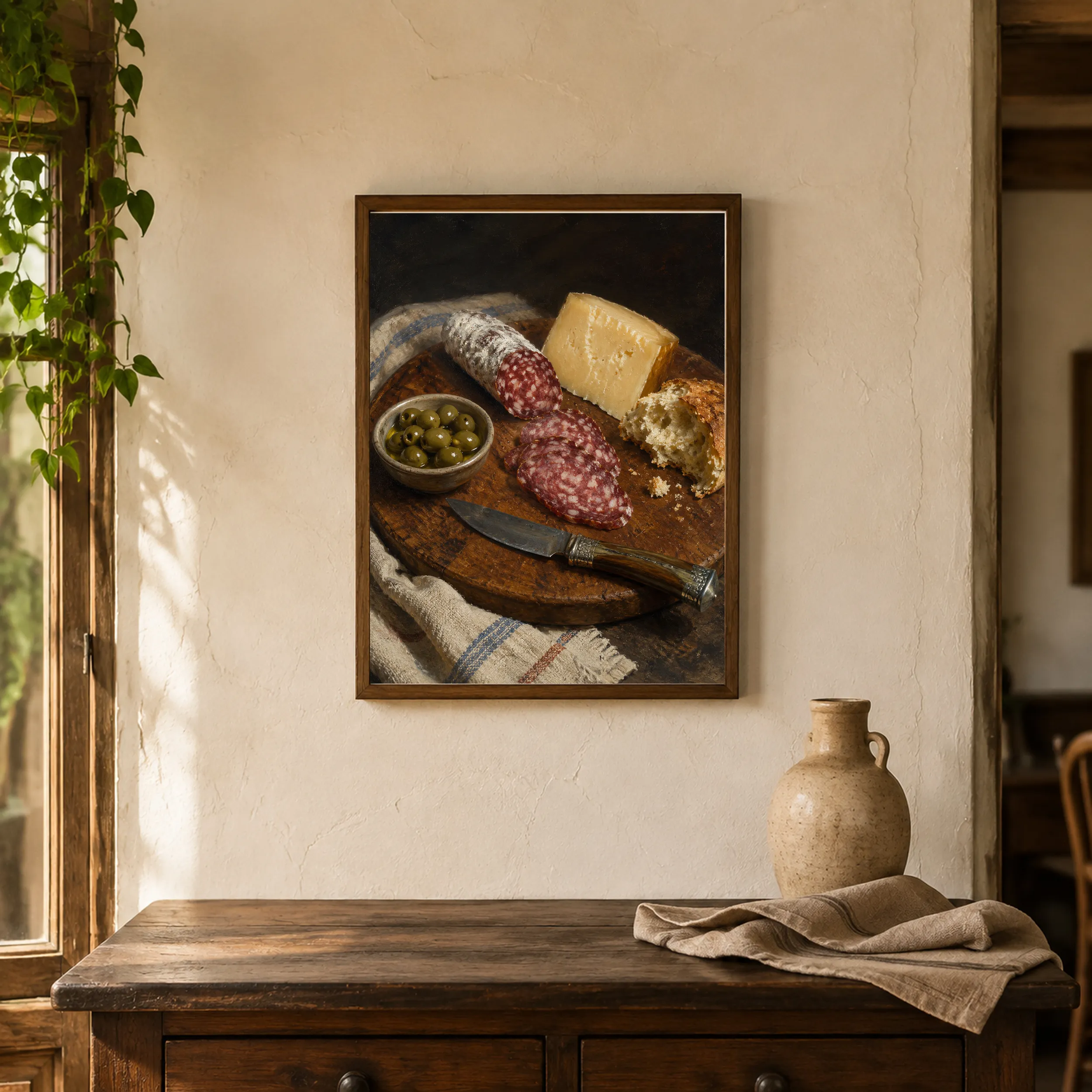 Framed print of salami, cheese and olives on a wooden board hanging in a warm interior.